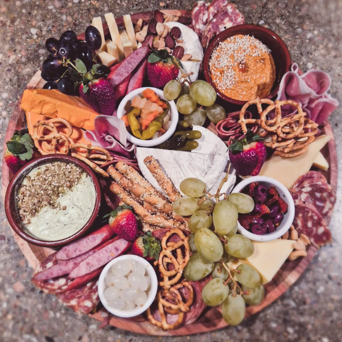 Overhead view of abundant grazing board with cheeses, cured meats, fresh fruit and dips on wooden board