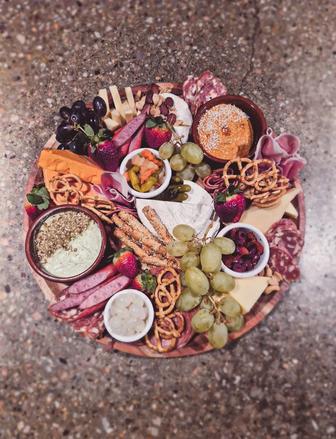 Overhead view of round grazing board with cheeses, meats, fruit and dips on granite floor