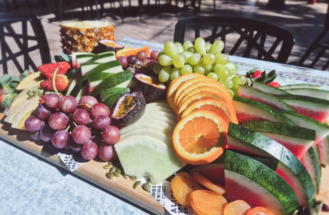Vibrant fruit platter with grapes, watermelon, oranges and tropical fruits on wooden board at outdoor event