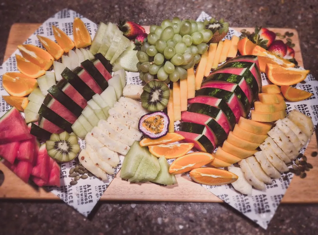Colourful fruit grazing board with striped arrangement of watermelon, grapes, kiwi, rockmelon and orange on wooden board